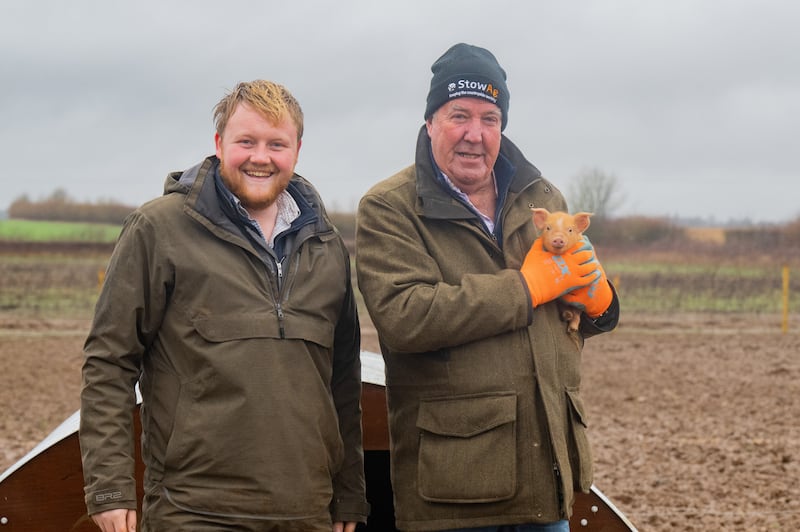 Jeremy Clarkson and Kaleb Cooper holding a piglet in a field