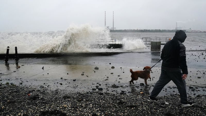 A man and a dog go for a walk as waves crash onto Clontarf promenade in Dublin (PA)