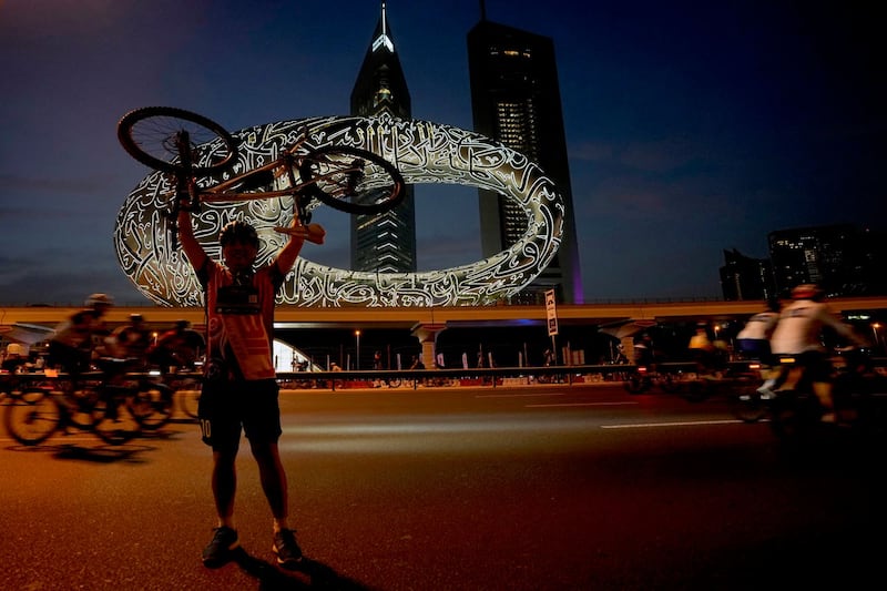 A cyclist poses for a photograph in front of the Museum of the Future and Emirates Towers, in Dubai 
