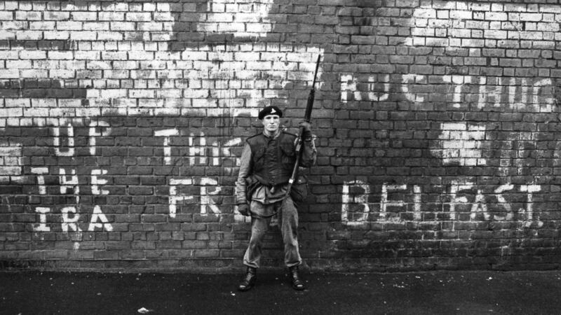 An armed British soldier on patrol in Belfast in 1971, standing against a wall with graffiti