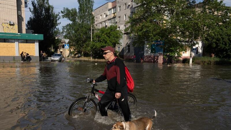 A local resident with a bike and a dog walks past buildings in Kherson, Ukraine, which were flooded after the Kakhovka dam was damaged overnight (Evgeniy Maloletka/AP)