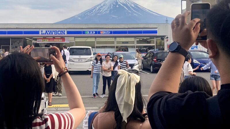 Visitors take a photo of Mount Fuji in front of a store (Kyodo News via AP)