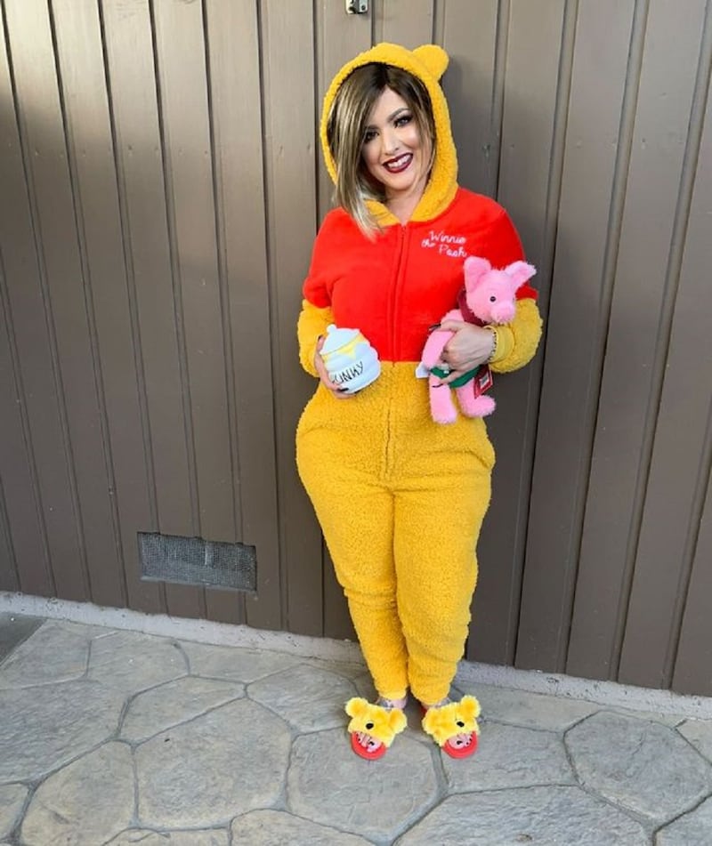 Woman wearing yellow and red onesie and holding a stuffed pink pig toy and a honey jar in her hands