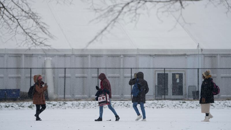 People walks across a snowy athletics field in front of a temporary shelter for migrants on Randall’s Island in New York (Seth Wenig/AP)
