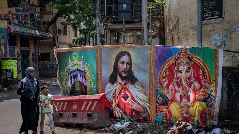 A Muslim woman and a boy walk past portraits of elephant-headed Hindu God Ganesha, Jesus Christ and Islam’s holy sites of Mecca and Medina, in the southern Indian city of Chennai (Altaf Qadri/AP)