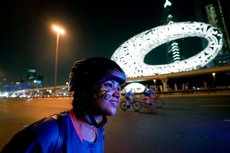 A cyclist with a bike painting on her face rides past the Museum of the Future in Dubai, United Arab Emirates