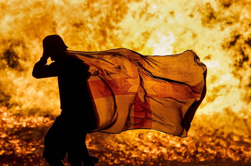 A young man carries a Northern Ireland flag in silhouette past the burning Craigyhill loyalist bonfire in Larne