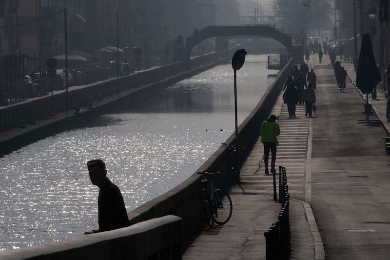 People walk along the Naviglio Pavese canal in Milan shrouded in mist and smog (Luca Bruno/AP)