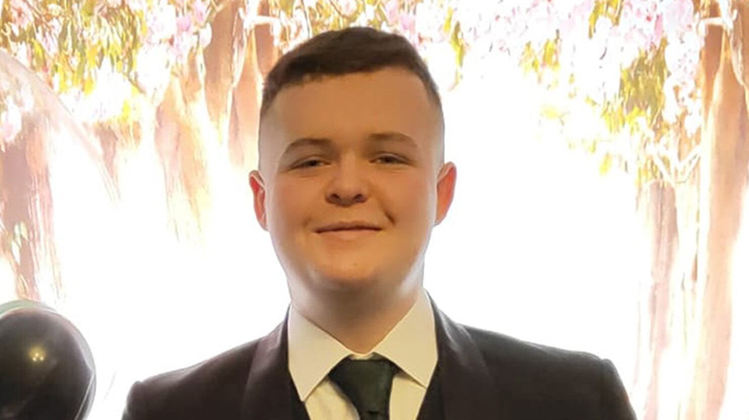 Jamie 'Jay' Marks standing beside balloons holding a champagne glass and wearing a suit