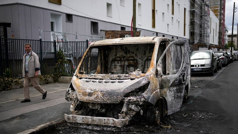 A man walks past a burned van in the aftermath of protests in Colombes, outside Paris (Christophe Ena/AP)