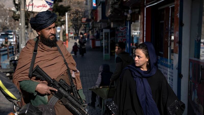 A Taliban fighter stands guard as a woman walks past in Kabul, Afghanistan (Ebrahim Noroozi/AP)