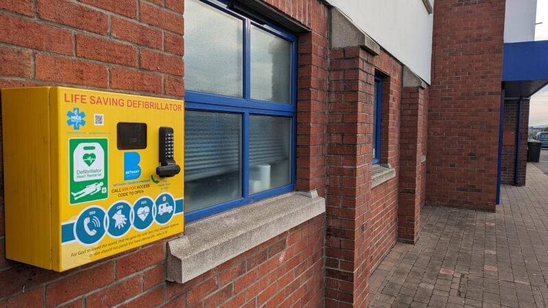A yellow defibrillator attached to a brick wall