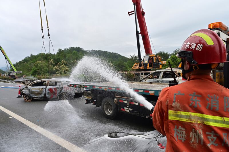 A firefighter sprays water on the remains of a car in the aftermath of the road collapse (Xinhua via AP)