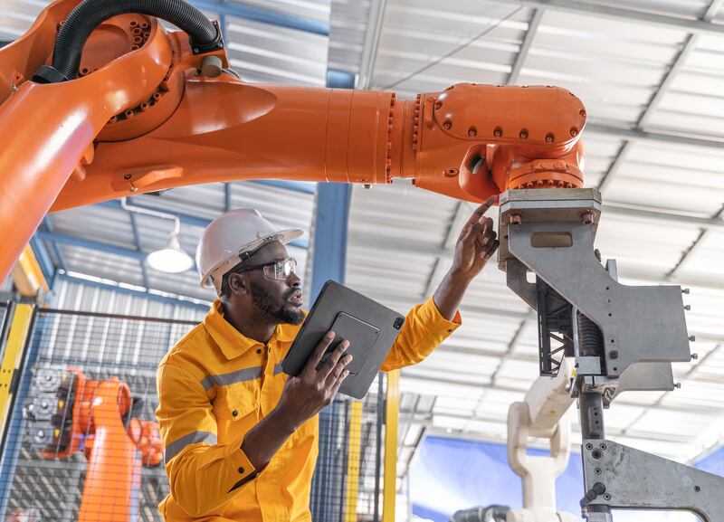 An engineer and tablet working with robotic arm at industrial manufacturing.