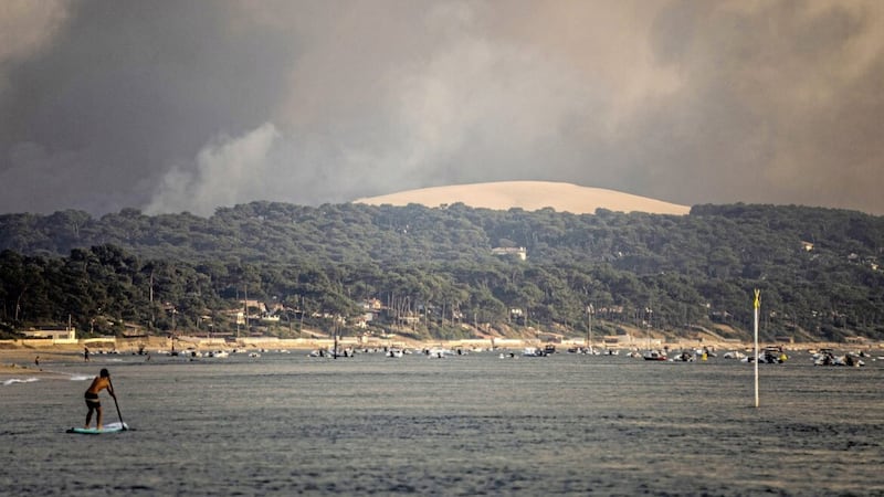 A paddle surfer is seen as smoke laden with ashes coming from a giant wildfire consuming the thousand-year-old forest bordering the Dune du Pilat rises over the beach of Pilat sur Mer, southwestern France on Monday. (AP Photo/Sophie Garcia) 