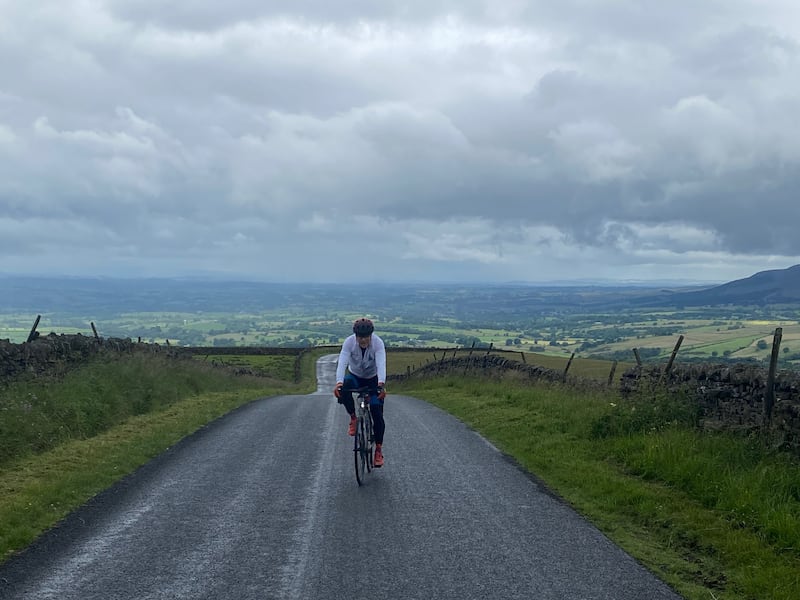 Pete Hawkins cycling over The Pennines with a scenic backdrop behind him
