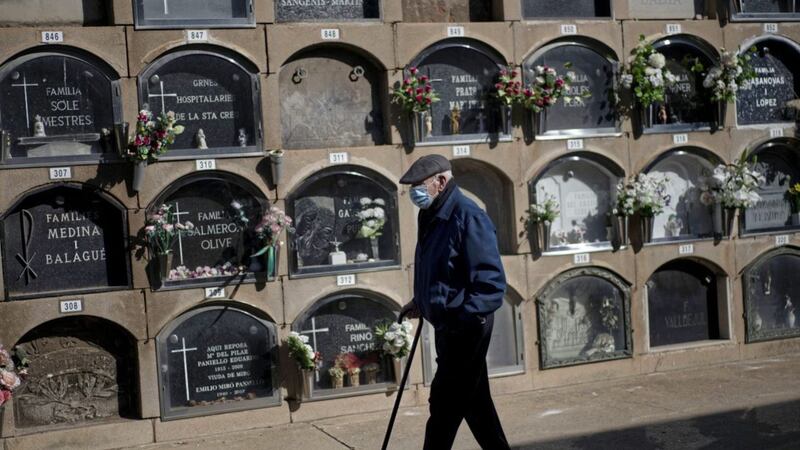 A man wearing a face mask, walks next to graves decorated with flowers in tribute of deceased relatives at a cemetery in Barcelona, Spain. November is a special month of remembrance. Picture by AP Photo/Emilio Morenatti 