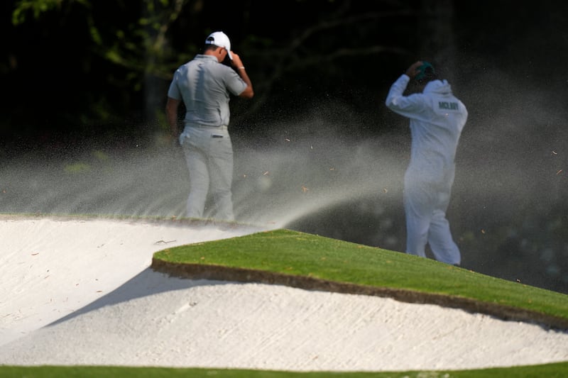 Rory McIlroy shield themselves from sand blown from bunkers on the 11th hole during the second round (Charlie Riedel/AP)