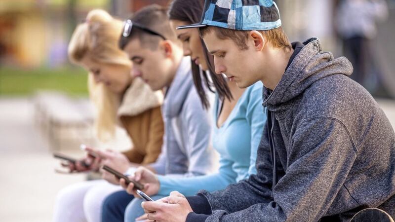 Group of teenagers sitting outdoors using their mobile phones 