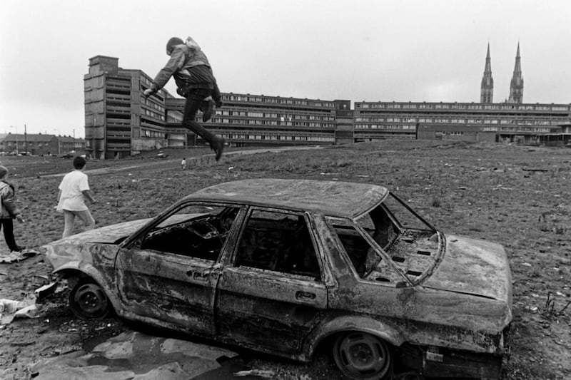 A boy jumping on a burnt-out car at Divis Flats in west Belfast in 1983. Picture by Martin Nangle 