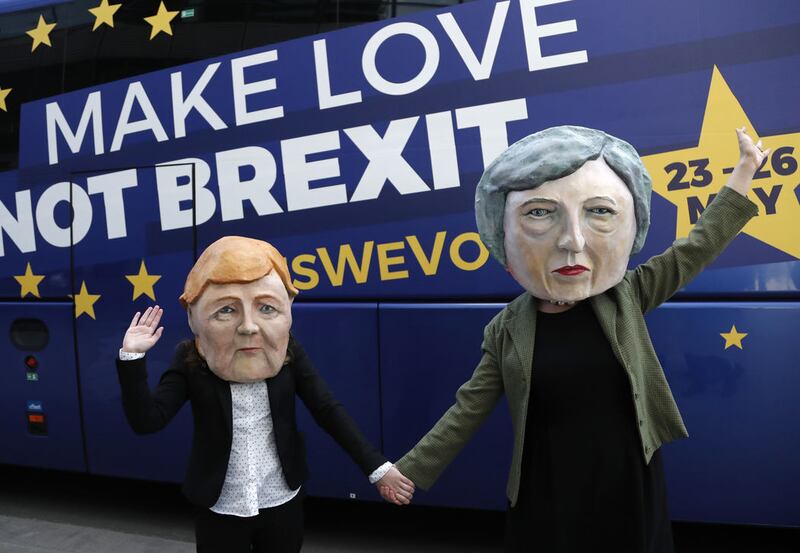 Activists pose with papier mache heads depicting British Prime Minister Theresa May, right, and German Chancellor Angela Merkel, left, during an anti-Brexit campaign stunt outside EU headquarters during an EU summit in Brussels, Thursday, March 21