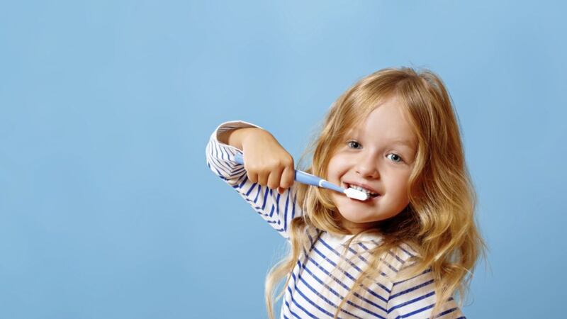 A little girl in striped pajamas is brushing her teeth with a toothbrush. The concept of daily hygiene. Isolated on a blue background 