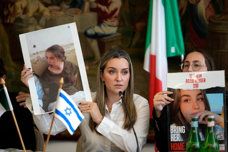 Ashley Waxman Bakshi, left, shows a photo of her cousin Agam Berger, one of the hostages being held by Hamas, flanked by Agam’s sister, Li-Yam Berger, during a press conference in Rome (Alessandra Tarantino/AP)