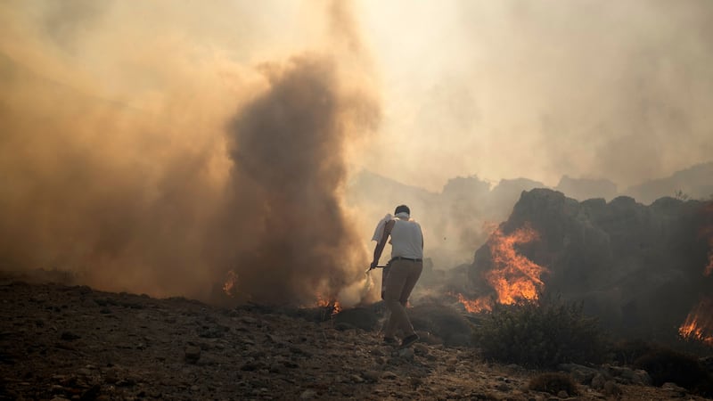 A local resident tries to extinguish a fire, near the seaside resort of Lindos (AP Photo/Petros Giannakouris)