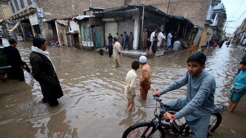 Youngsters wade through a flooded street caused by heavy rain in Peshawar, Pakistan (Muhammad Sajjad/AP)
