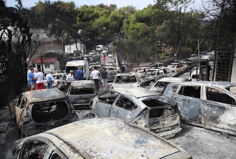 People stand amid the charred remains of burned-out cars in Mati, east of Athens, Greece, in July 2018 (Thanassis Stavrakis/AP)