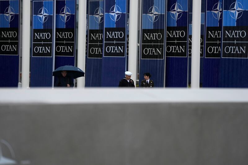 Two military personnel walk past Nato banners prior to a wreath-laying ceremony at Nato headquarters in Brussels (Virginia Mayo/AP)