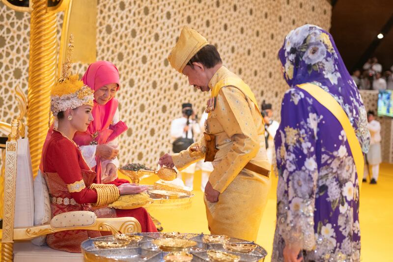 Brunei’s Sultan Hassanal Bolkiah, centre right, pouring scented oil on the hands of Prince Abdul Mateen’s bride Yang Mulia Anisha Rosnah, left, during the royal powdering ceremony at Istana Nurul Iman (Brunei’s Information Department via AP)