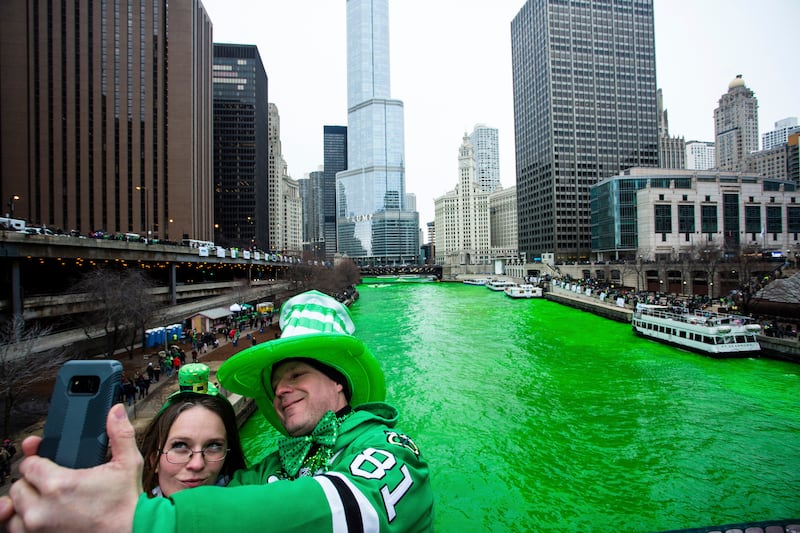 Two people take a photo in front of the green Chicago River on St Patrick's Day