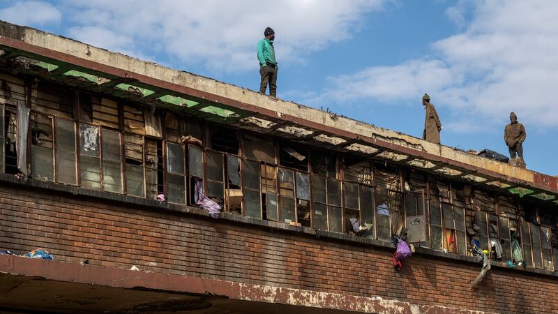 Squatters stand on a rooftop overlooking the scene of one of South Africa’s deadliest inner-city fires in Johannesburg (Jerome Delay/AP)