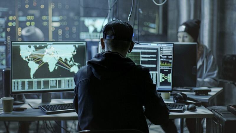 Back View of Teenage Hacker Working in Computer and Infecting with Virus Data Servers of Government Infrastructures. His Hideout is Dark with Many Monitors Around. 