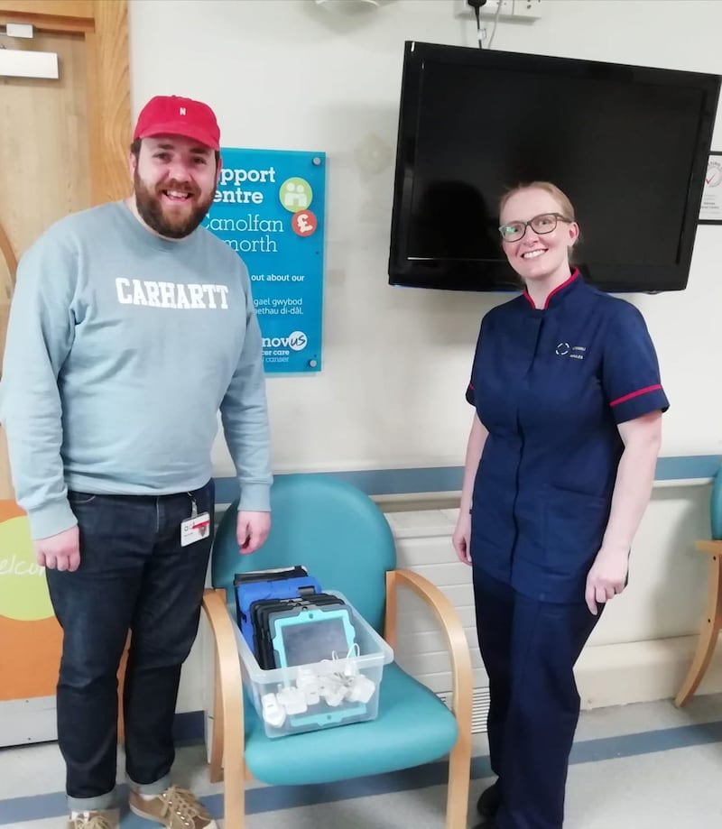Undated handout photo issued by Velindre Cancer Centre of Matthew Burnett, Head of Operations & Contracts at ACT handing over 10 iPads to Velindre Cancer Centre nurse Amy Mumford