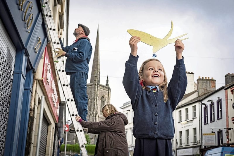 Five-year-old Thea Johnston from Enniskillen Integrated Primary helps artists Simon Carman and Helen Sharp as they begin the installation of 150 golden swallows in and around the town. Picture by Brian Morrison 