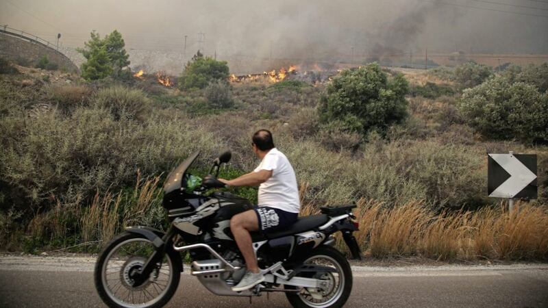 A motorcyclist looks at smoldering shrubbery on a road near Kineta, west of Athens, on Monday. Residents were fleeing their homes as a swift-moving fire blazed through a mountainous pine forest west of Athens and churned out smoke that turned the sky orange over the Greek capital PICTURE: Thanassis Stavrakis/AP 
