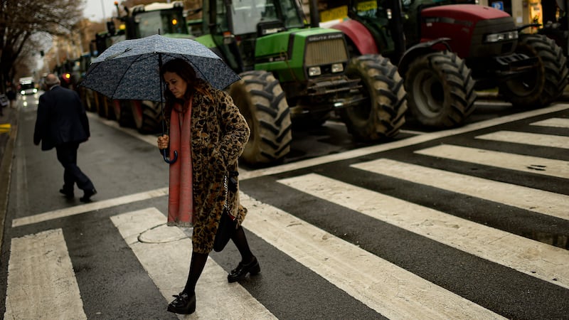 A woman crosses a street as farmers in tractors protest in Pamplona, northern Spain (Alvaro Barrientos/AP)