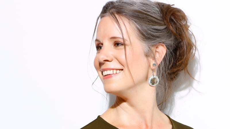 Image of Emily Gray in a green dress in front of a white background. Her hair is tied in a ponytail and she is smiling.