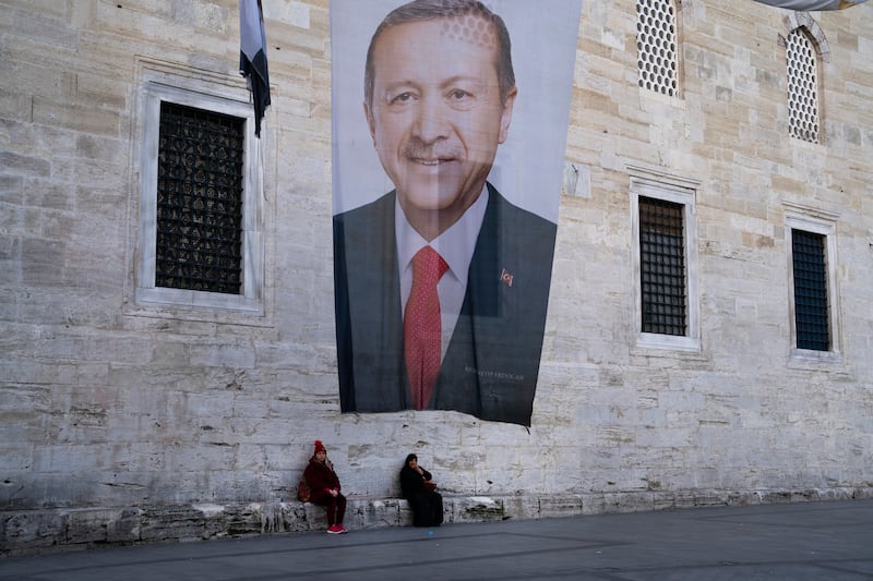 Two women sit near a campaign banner of Turkish President Recep Tayyip Erdogan (Francisco Seco/AP)