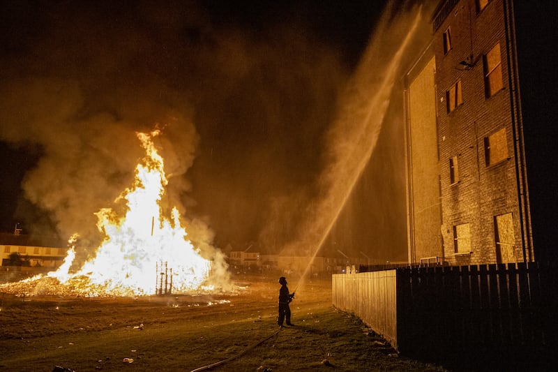 A firefighter from Northern Ireland Fire and Rescue Service hose down an apartment block close to the burning of the loyalist Corcrain bonfire in Portadown, Co Armagh, lit to usher in the Eleventh night ahead of the Twelfth commemorations. Picture by Liam McBurney, PA 