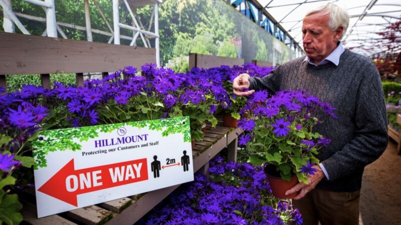 Robin Mercer, owner of Hillmount Garden Centres, tending to a potted plant beside a sign advising customers about social distancing. Picture by Liam McBurney, Press Association