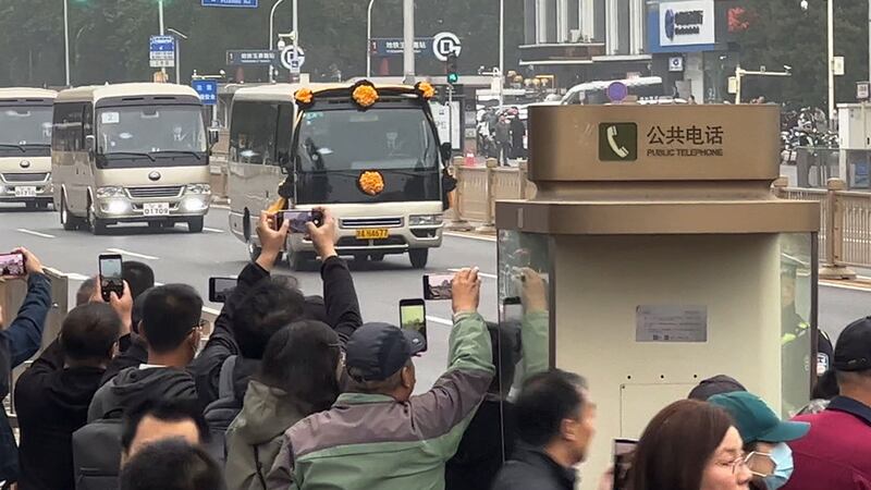 People use their smartphones to film a bus festooned with flowers believed to be carrying the body of former premier, Li Keqiang (AP Photo)