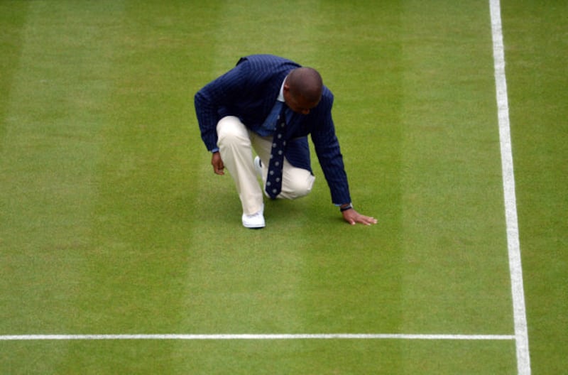 The umpire checks the moisture on the grass during the match between Dan Evans and Alexandr Dolgopolov on day Three of the Wimbledon Championships at the All England Lawn Tennis and Croquet Club, Wimbledon.