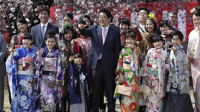 Japanese Prime Minister Shinzo Abe, centre, poses for a group photo with members of Japanese pop group Momoriro Clover Z and Japanese child actors wearing Japanese kimono during a cherry blossom viewing party hosted by Abe at Shinjuku Gyoen National Garden in Tokyo on Saturday 