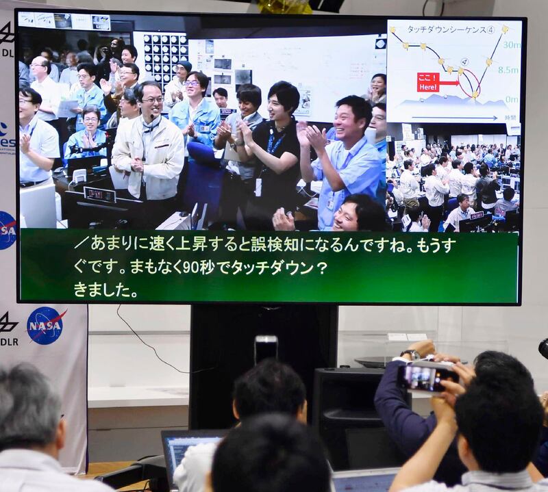 A monitor shows Hayabusa2 project team members celebrating the spacecraft's second touchdown on an asteroid in the control room in Japan