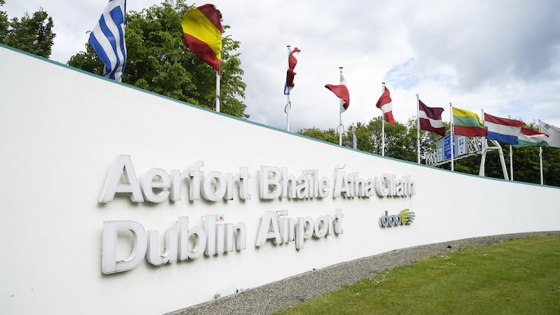 A view of the sign outside Dublin airport reading 'Aerfort Bhaile Átha Cliath - Dublin Airport' with a range of flags on top