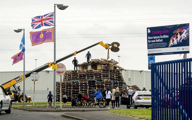 A crowd gathers to watch men  remove material from a July 11th night bonfire at Avoniel Leisure Centre shortly after a Belfast City Council committee voted to send contractors in to remove material. Picture by PA Wire