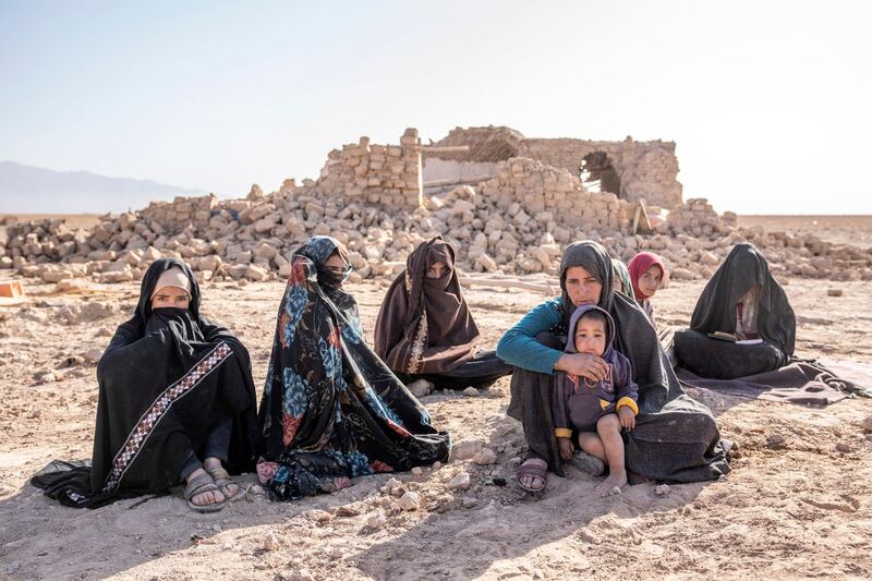Afghan women sit in front of houses that were destroyed
